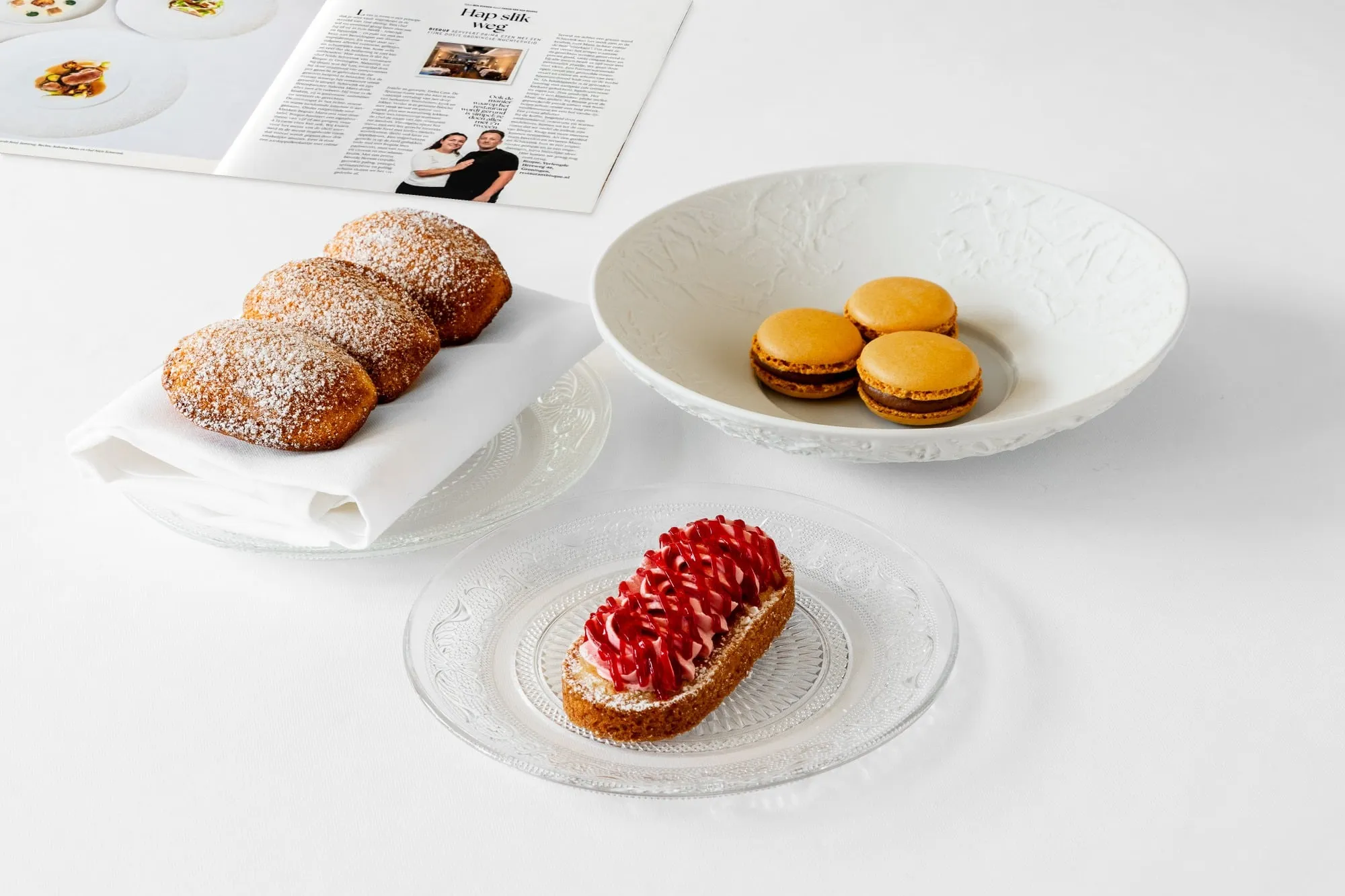 Drie gebakjes met poedersuiker, macarons in een kom en een gebakje met rood glazuur