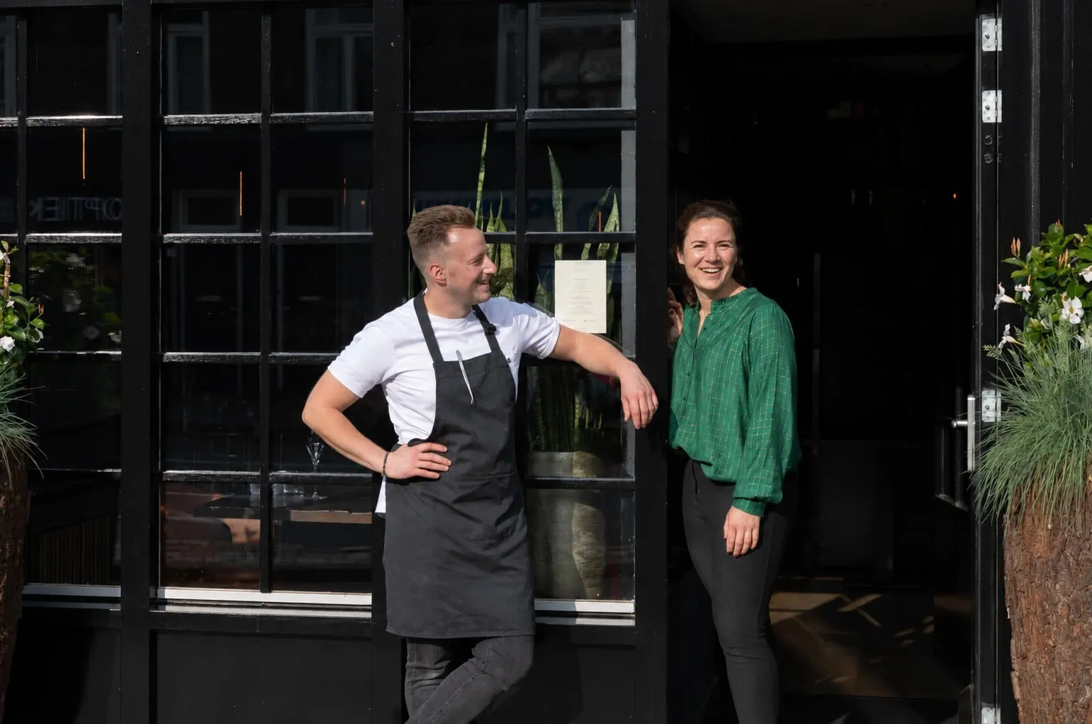 Cook in an apron and a woman in a green blouse at the open door of the façade