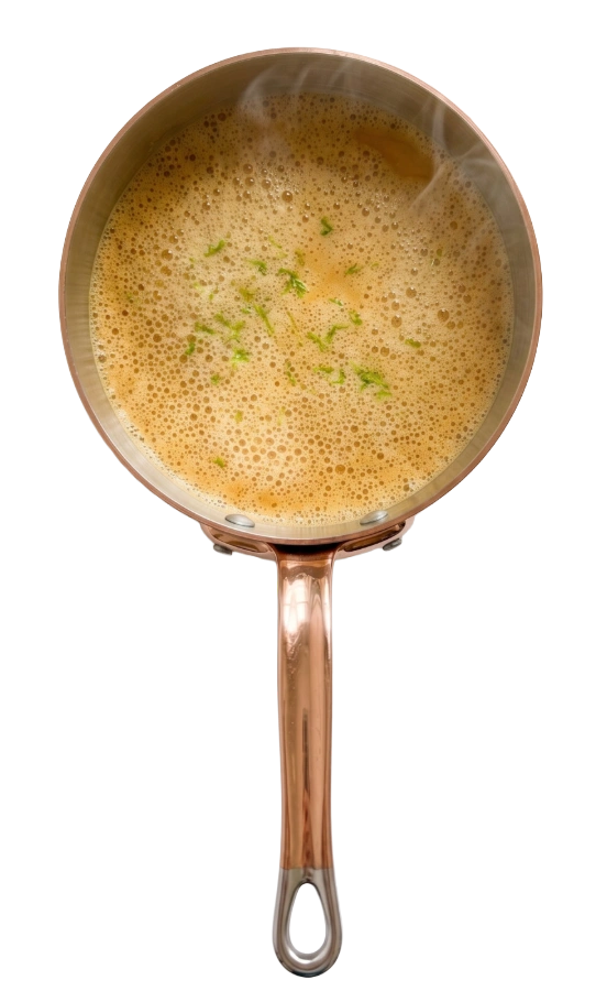 Koperen steelpan met schuimende bisque, bestrooid met fijngesneden groene kruiden