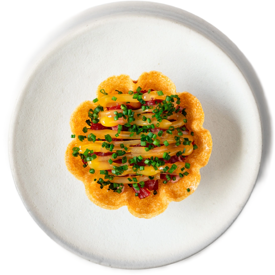 A crisp flower-shaped case filled with yellow and red strips and chives, on a white plate