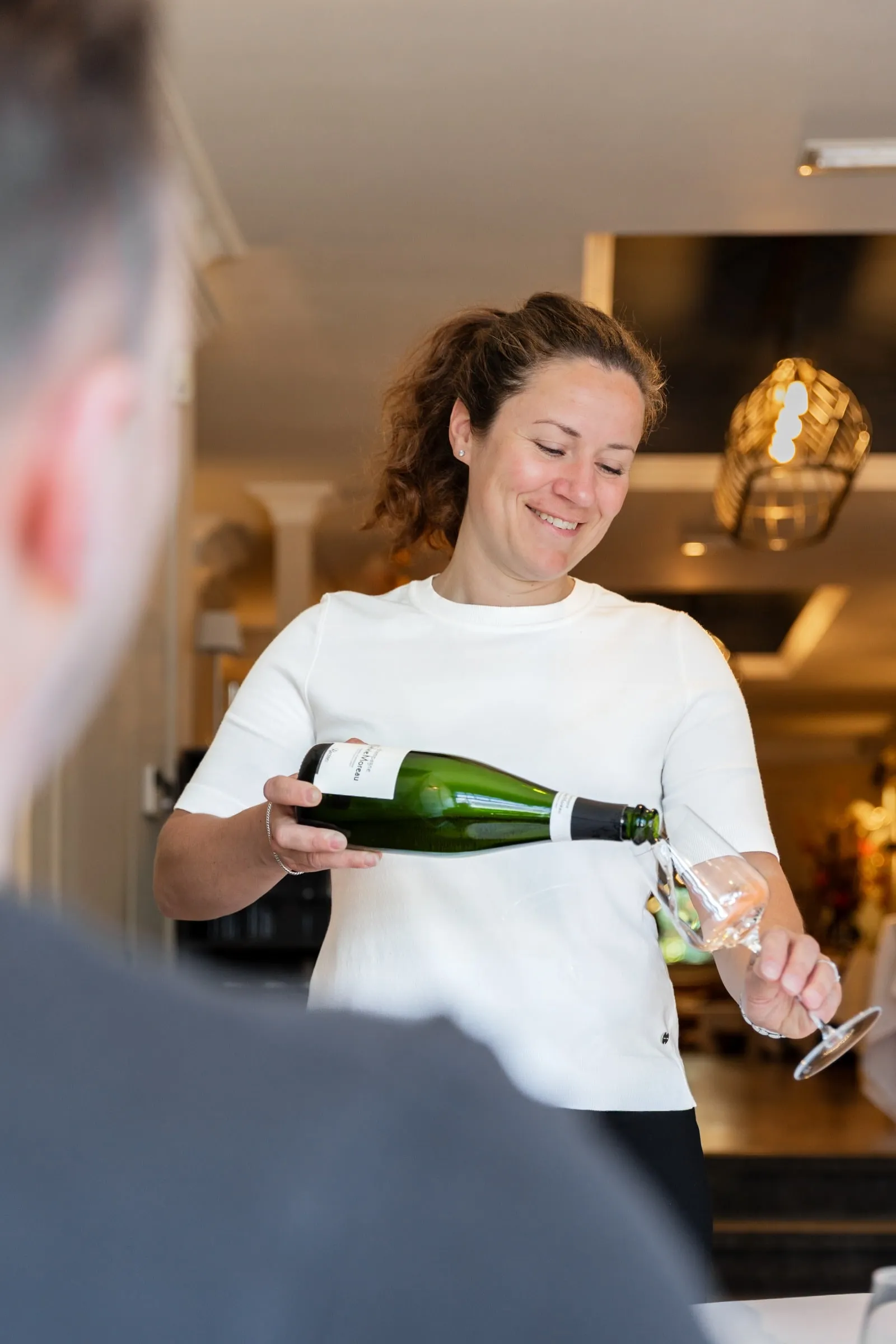 Medewerker schenkt mousserende wijn in een glas dat ze zelf vasthoudt.
