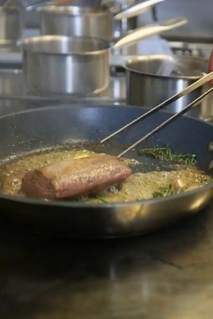 Niels sears a piece of meat in the pan, on the stove in the kitchen at Bisque