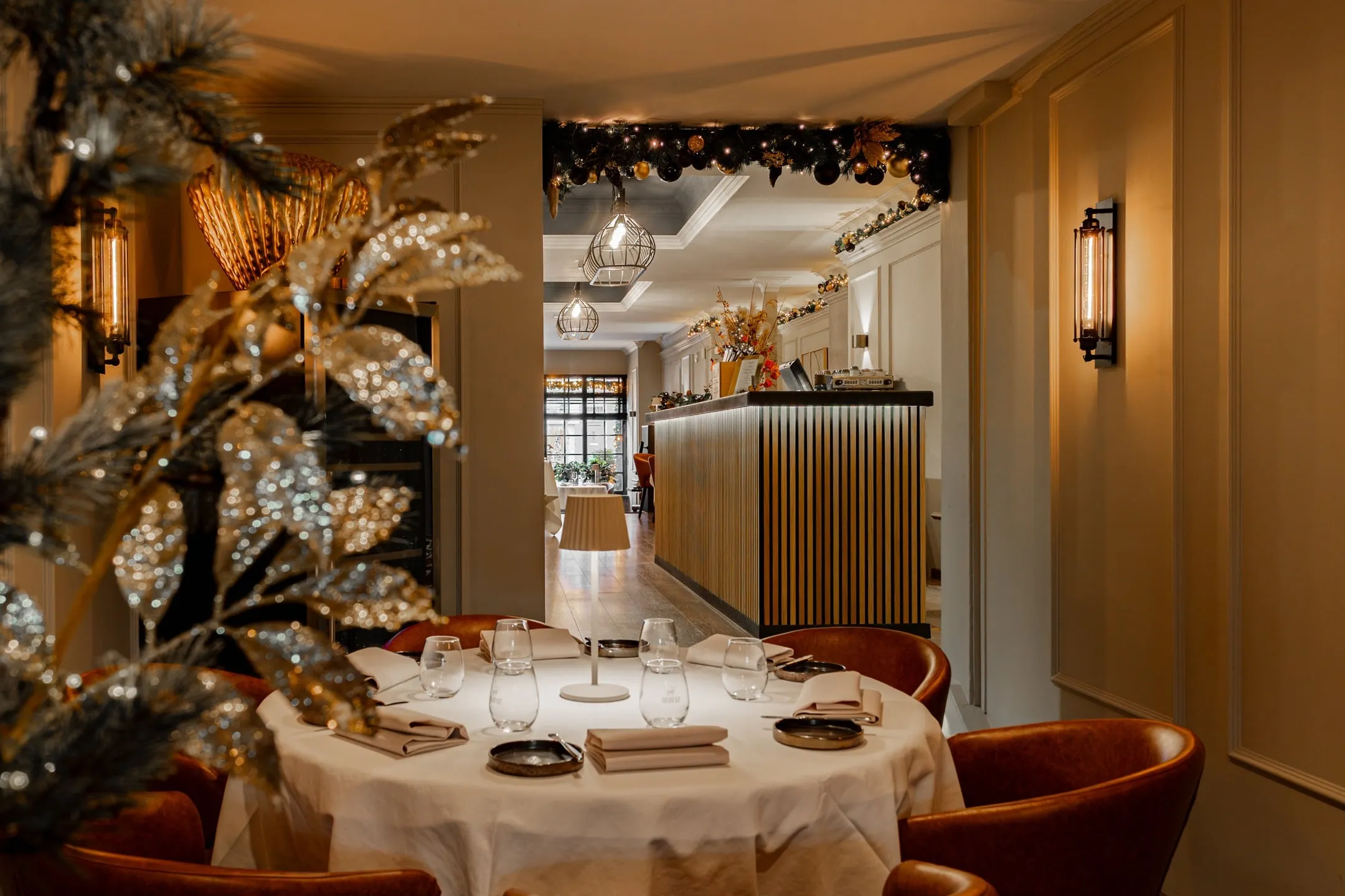 Ronde tafel met wit kleed, daarachter de bar en een kerstguirlande boven de doorgang
