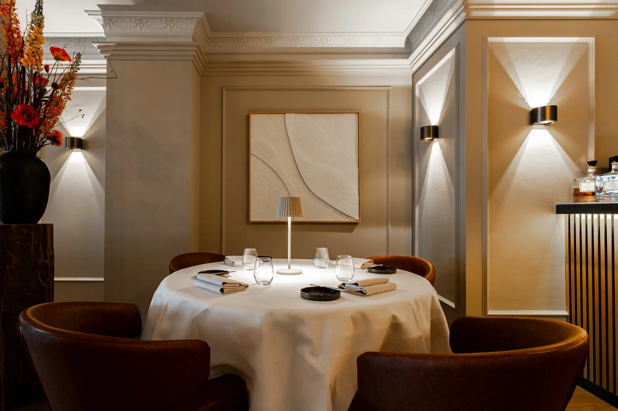 Round table with a white cloth and four brown leather armchairs, wall lamps and a plastered ceiling