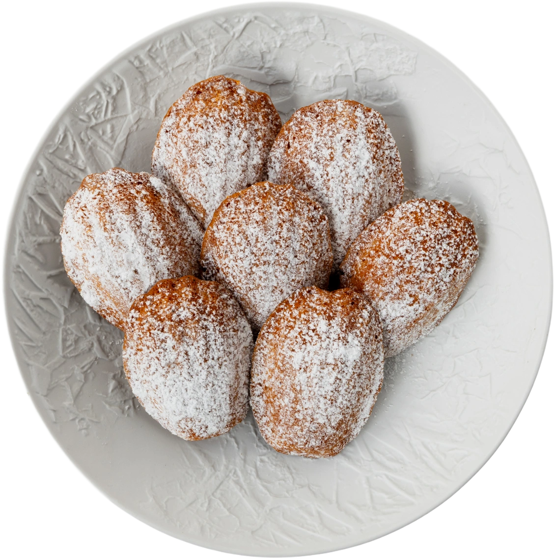 Zeven madeleines met poedersuiker op een wit bord met reliëf